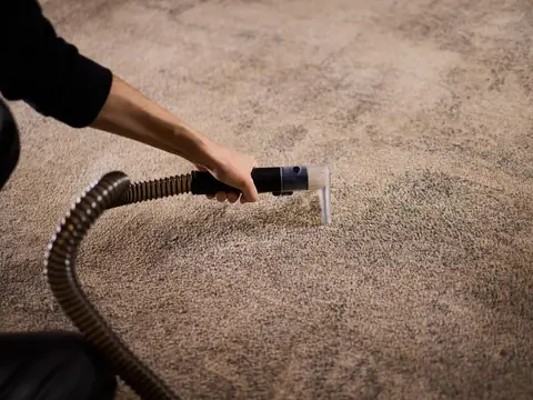 A hand holding a clear extraction nozzle on a ribbed hose against a beige carpet