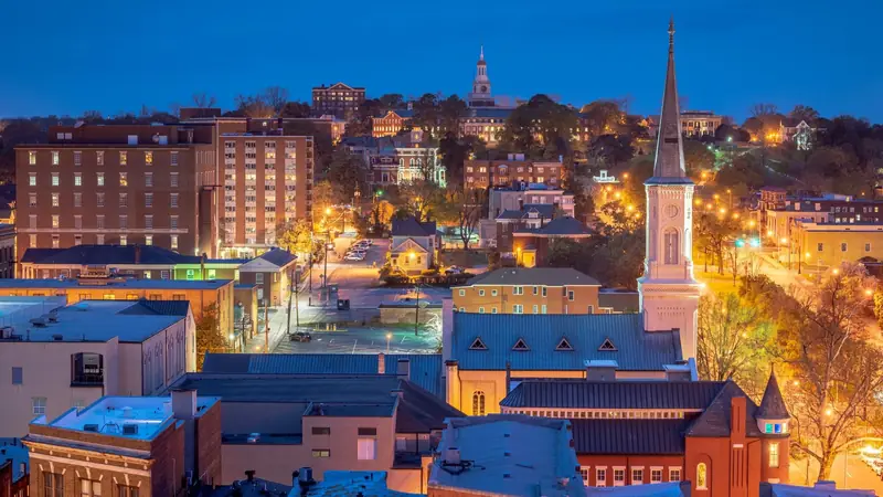 Downtown Macon, Georgia at dusk seen from above: brick buildings, a white church steeple and a clock tower on the hill under a deep blue sky